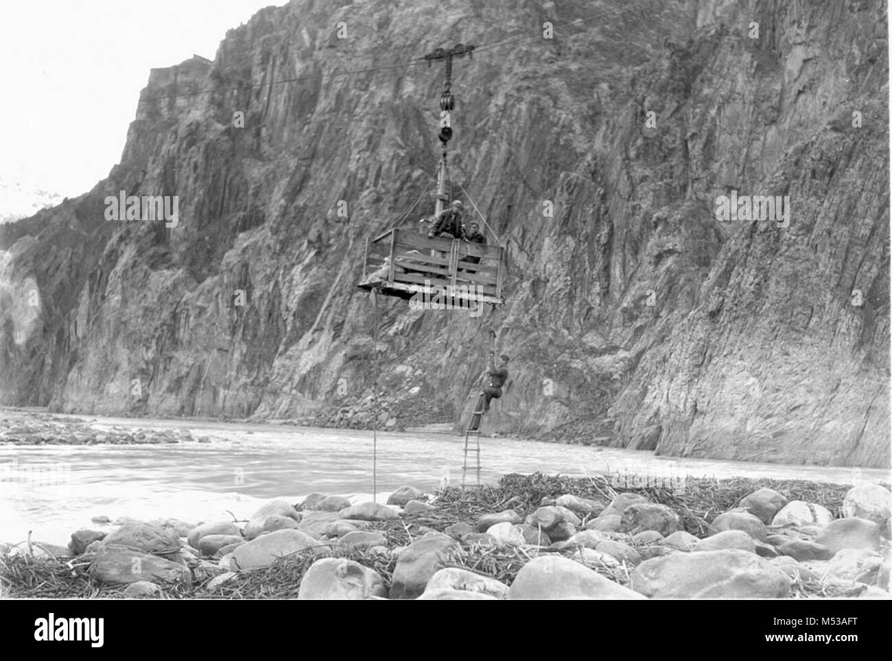 Dettaglio di CCC ENROLLEES sospeso sopra il fiume Colorado nel cavo di una vettura tranviaria. L'uomo appeso al di sotto del tram auto da una scaletta di corda. CIRCA 1936. Grand Canyon Parco Nat storica sul fiume foto. Foto Stock