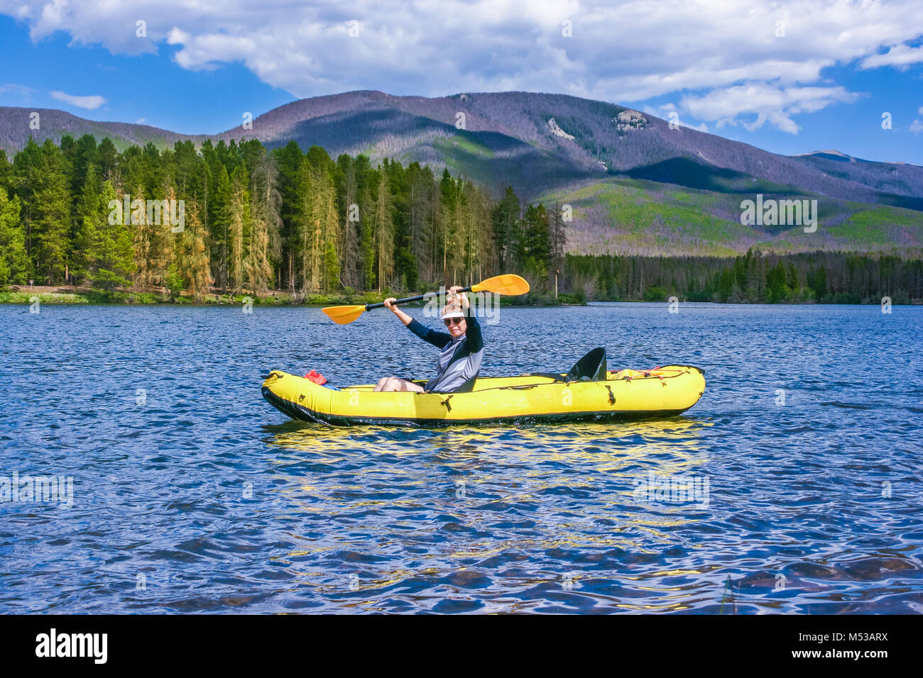 Donna di mezza età divertirsi sul lago in kayak gonfiabili; foreste e montagne sullo sfondo; Colorado, STATI UNITI D'AMERICA Foto Stock