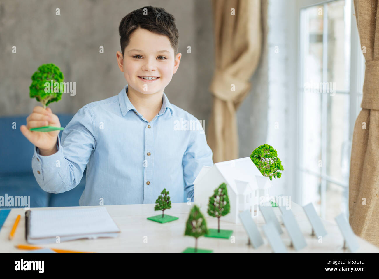 Piacevole boy in posa con albero in miniatura modelli Foto Stock