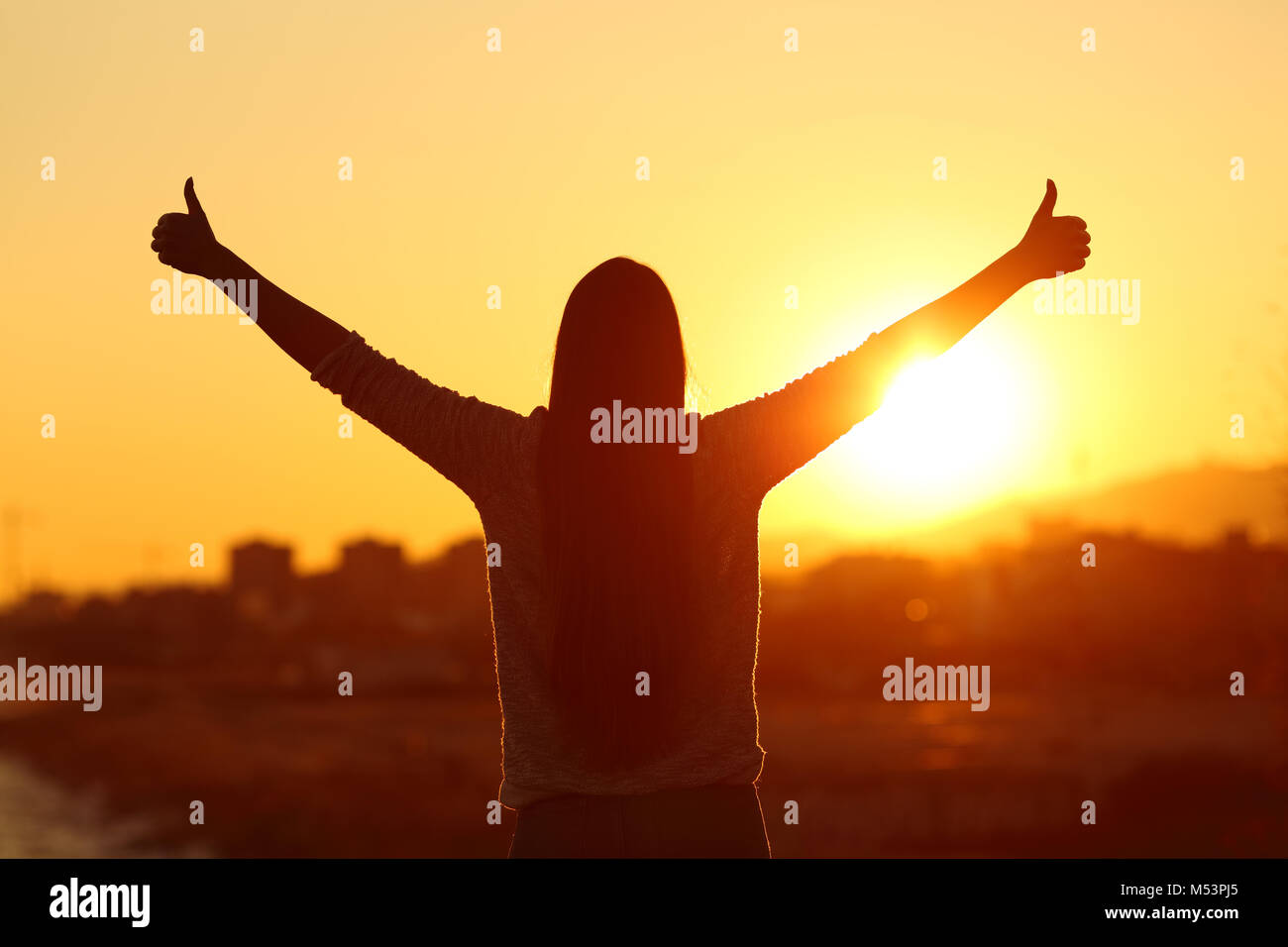 Vista posteriore retroilluminazione silhouette di donna bracci di sollevamento con il pollice su per il sole al tramonto Foto Stock