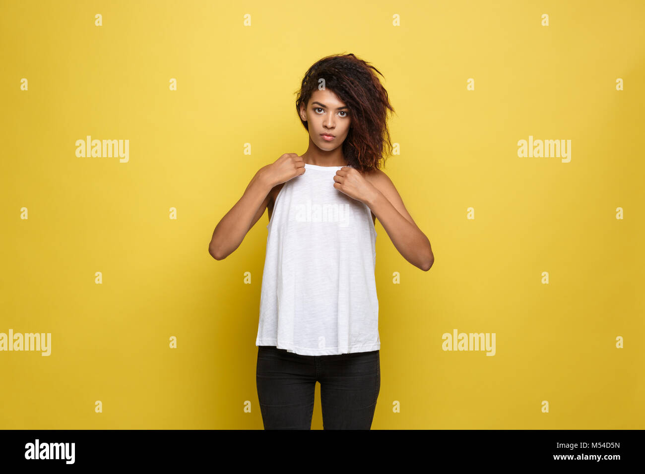 Bella attraente americano africano donna posting e vestito in su la sua t-shirt bianco. Il giallo di sfondo per studio. Spazio di copia Foto Stock