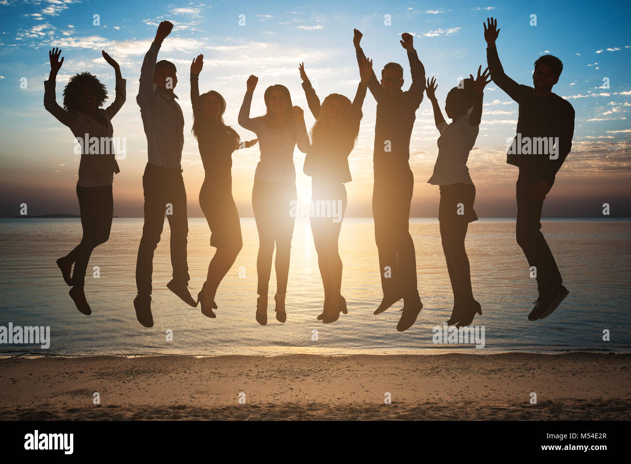 Silhouette di Persone che saltano insieme sulla spiaggia durante il tramonto Foto Stock