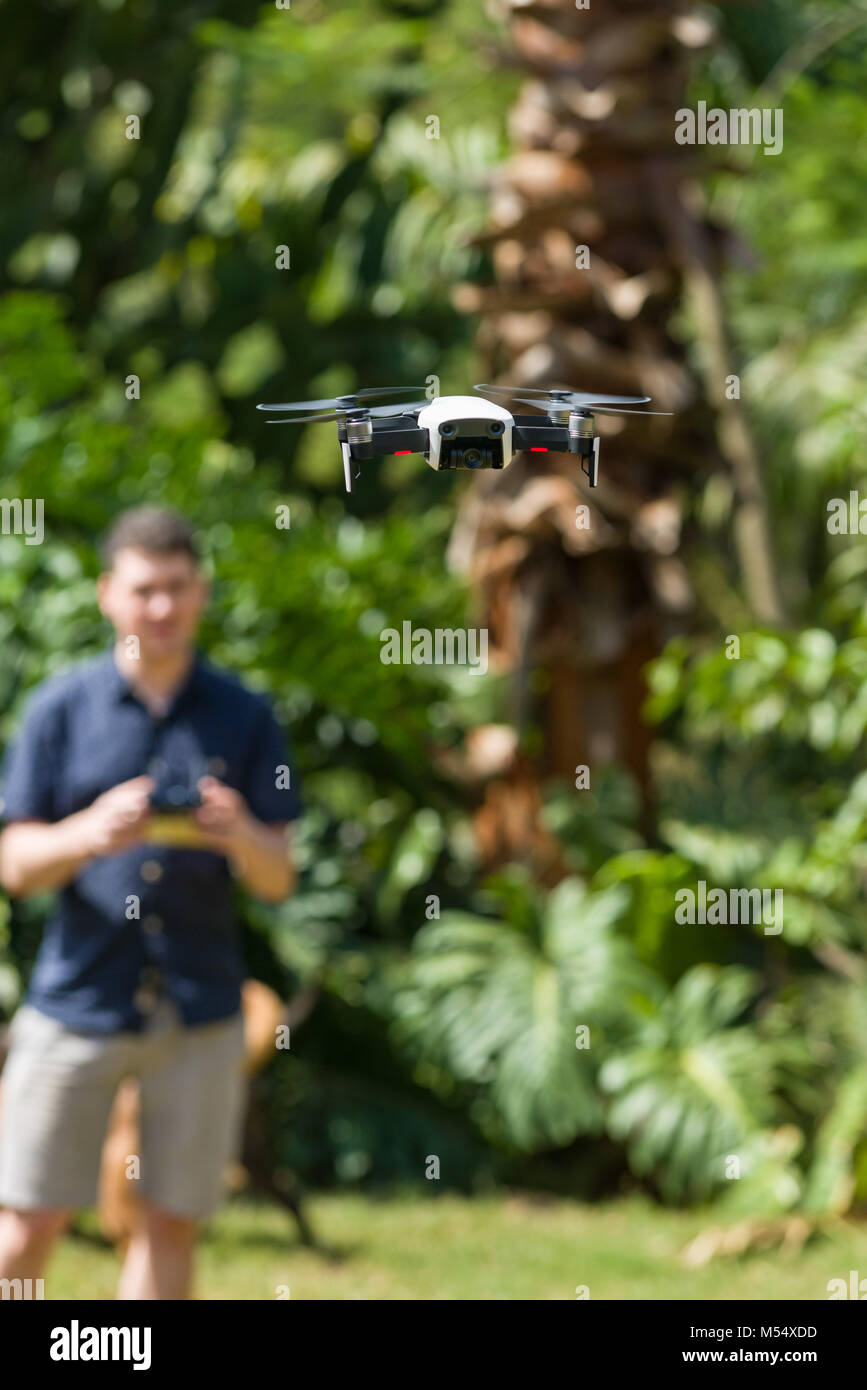 Un DJI Mavic aria drone in volo con un uomo che lo controlla in background Foto Stock