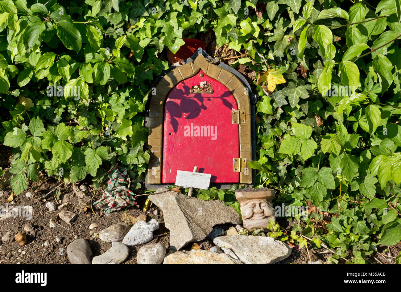 Rosso porta anteriore di un gnome casa circondata da edera Foto Stock