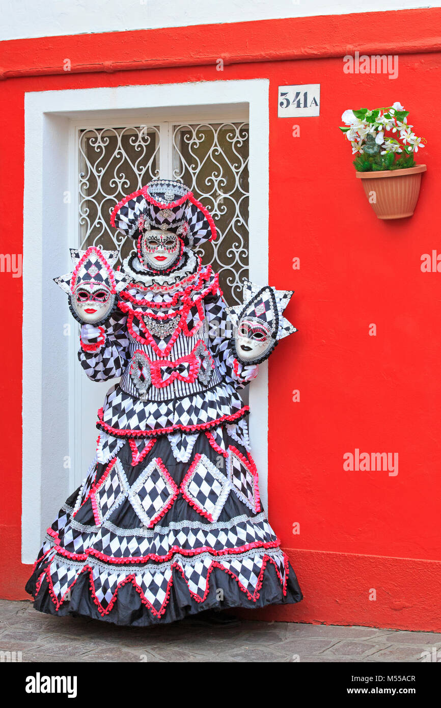 Una donna mascherata al di fuori di una casa tradizionale durante il Carnevale di Venezia (Carnevale di Venezia) a Burano, Italia Foto Stock