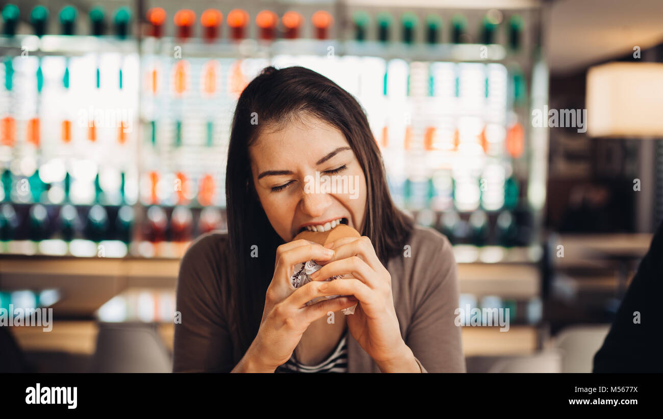 Giovane donna mangiare hamburger grassi.Craving fast food.godendo colpevole piacere,mangiare cibo spazzatura.soddisfatto l'espressione.rompendo la dieta regole,rinunciare a dieta Foto Stock