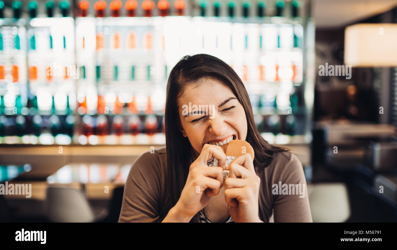 Giovane donna mangiare hamburger grassi.Craving fast food.godendo colpevole piacere,mangiare cibo spazzatura.soddisfatto l'espressione.rompendo la dieta regole,rinunciare a dieta Foto Stock