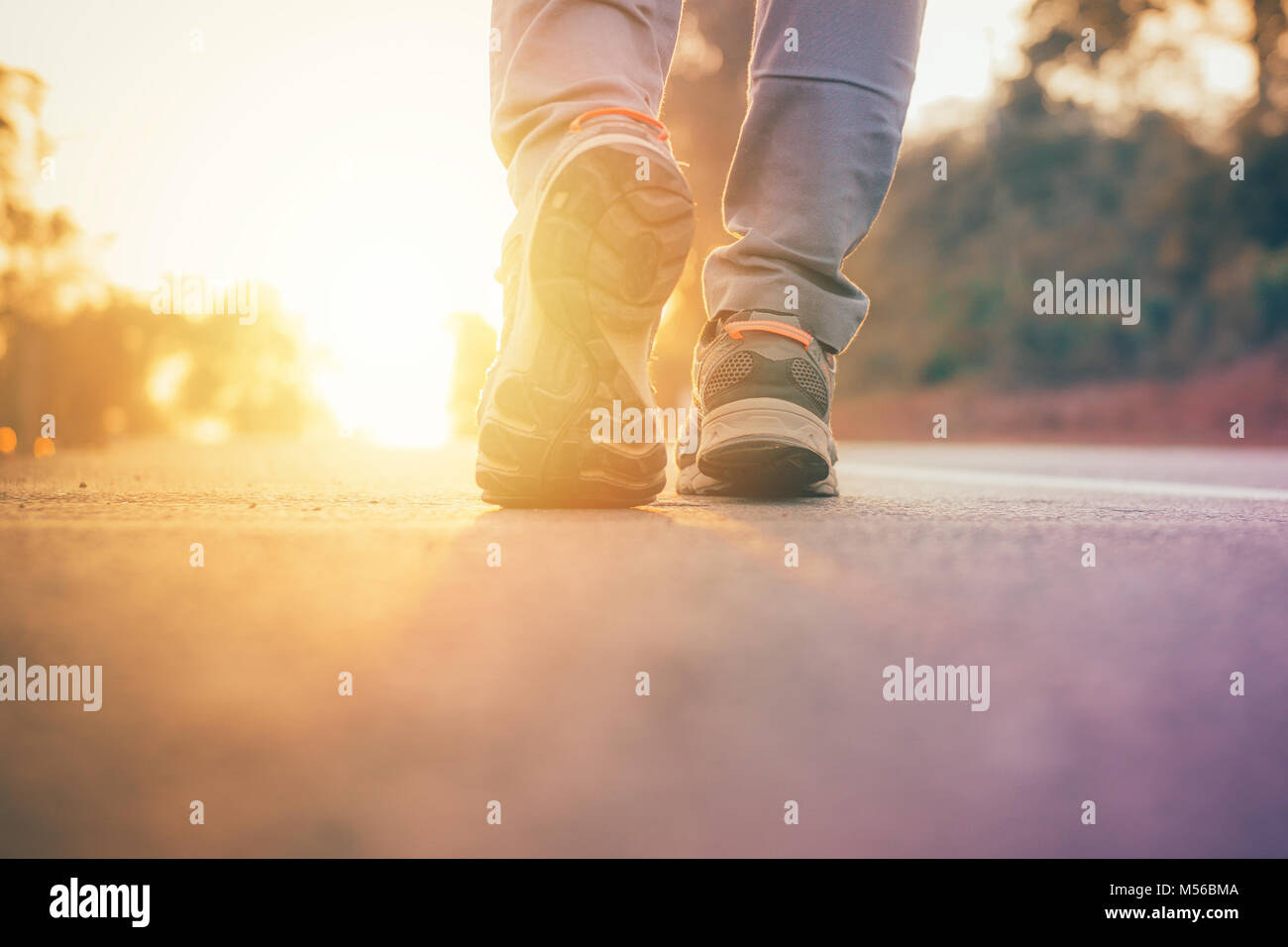 Uomo che cammina sulla strada con luce solare flare ,close up su scarpe da jogging wellness allenamento dopo il lavoro Foto Stock