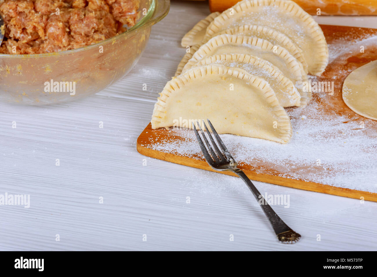 Non torrefatto cheburek con la farina su una tavola di legno. Sfondo nero. Foto Stock