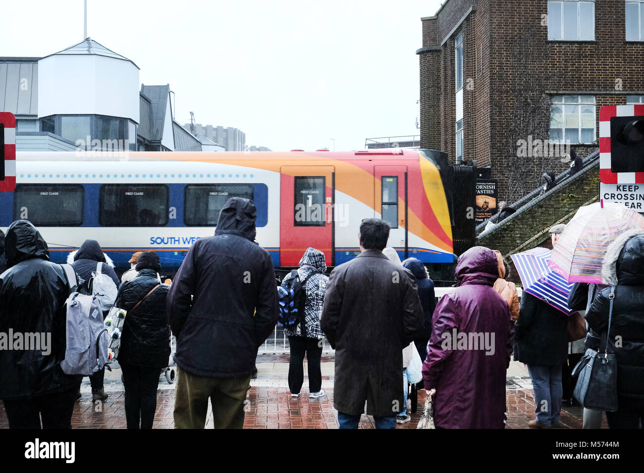 A sud ovest il treno passa attraverso un passaggio a livello attraverso una trafficata strada alta. La pista è barriered off mentre i pedoni attendere a croce Foto Stock