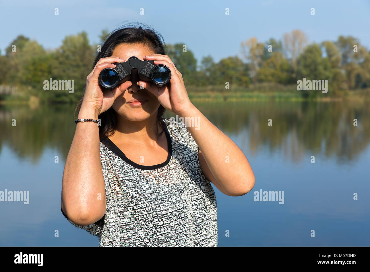 Donna che guarda attraverso il binocolo a waterfront Foto Stock
