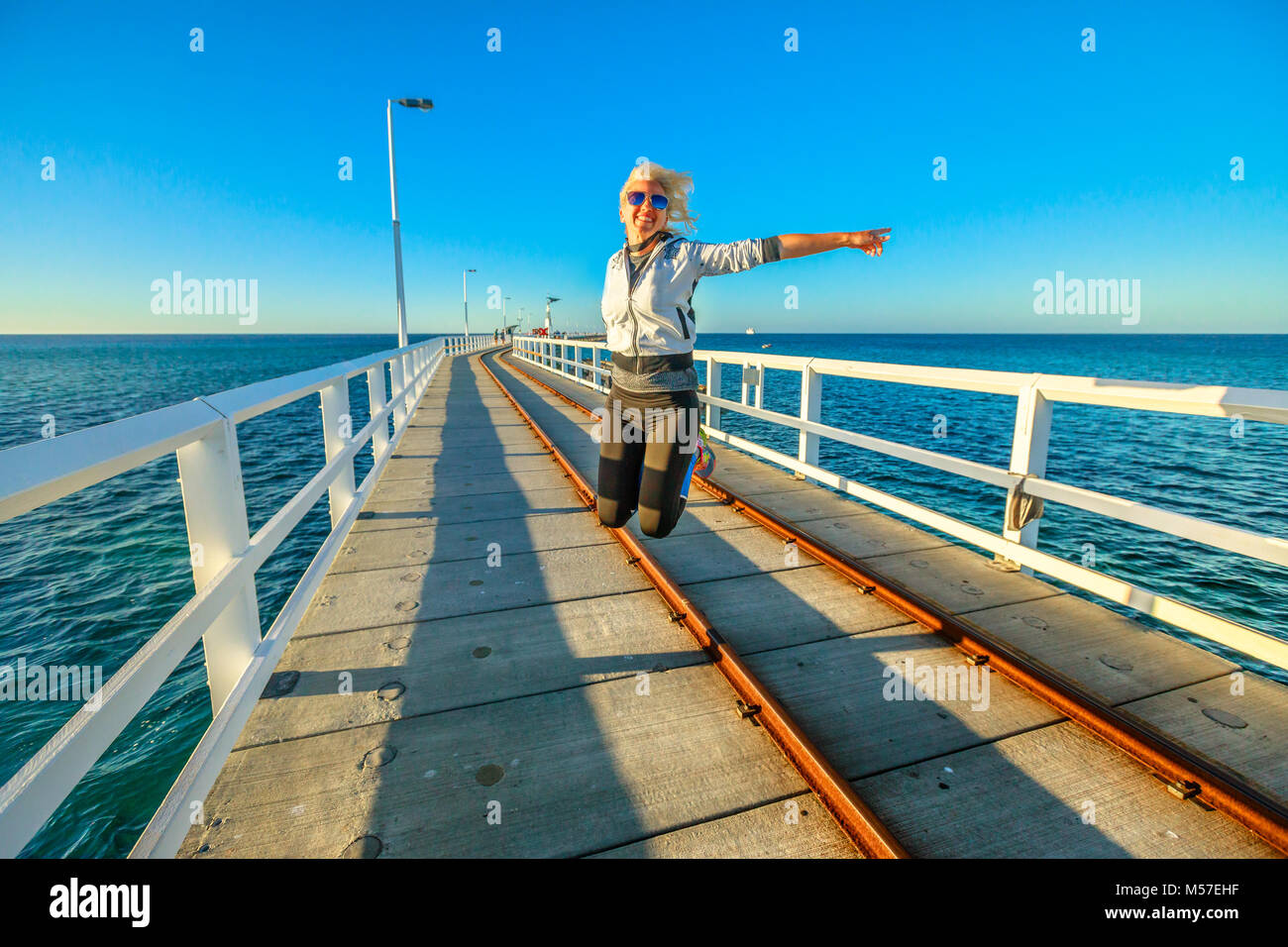 Australia occidentale la libertà di viaggio concetto. Felice donna caucasica saltando al Busselton Jetty in Busselton, Western Australia. Femmina su ponticello iconico molo in legno in WA, Australia. Foto Stock