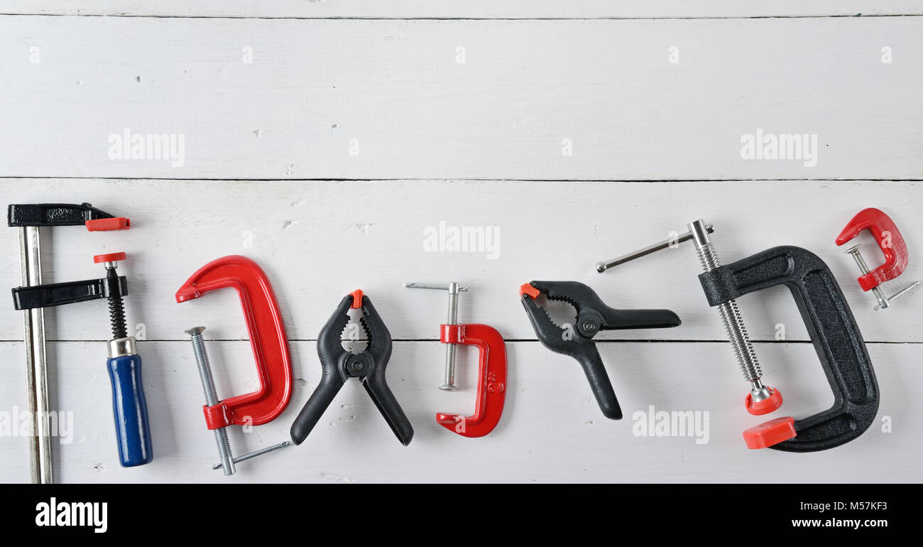 Impostare le fascette di fissaggio per legno e parti di metallo bianco su una superficie di legno. Strumenti sfondo. Vista dall'alto. Copia dello spazio. Foto Stock
