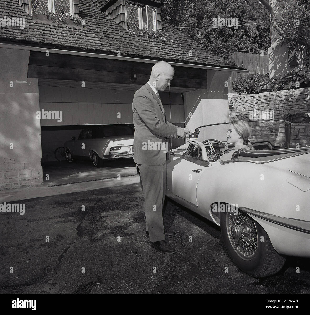 Anni sessanta, STATI UNITI D'AMERICA, storico, venditore consegna ad una signora al volante di un open-top Jaguar auto sportiva, i più recenti accessori per automobile, un dispositivo di controllo remoto che si apre automaticamente le porte di garage, Los Angeles, California. Foto Stock