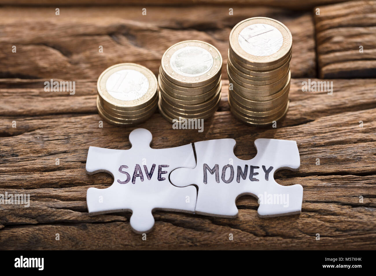 Primo piano di risparmiare denaro jigsaw pezzi di monete impilate su legno Foto Stock