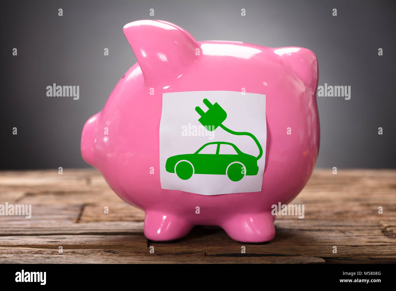 Primo piano di verde auto elettrica in rosa piggybank su legno Foto Stock