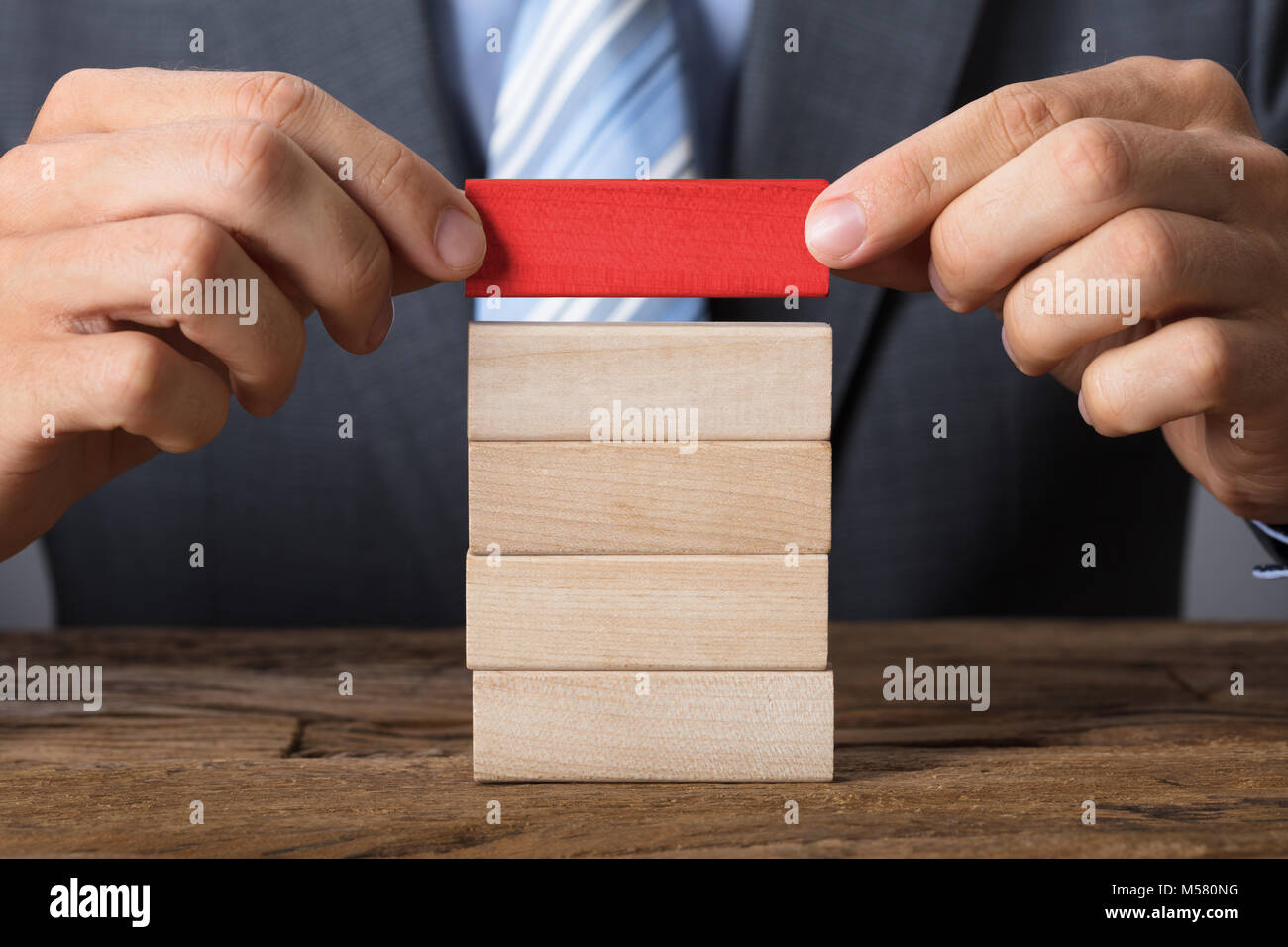 Vista dettagliata sezione mediana di imprenditore immissione blocco rosso sulla torre di legno a tavola Foto Stock
