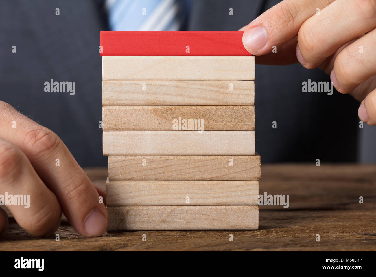 Vista dettagliata sezione mediana di imprenditore immissione blocco rosso sulla torre di legno a tavola Foto Stock