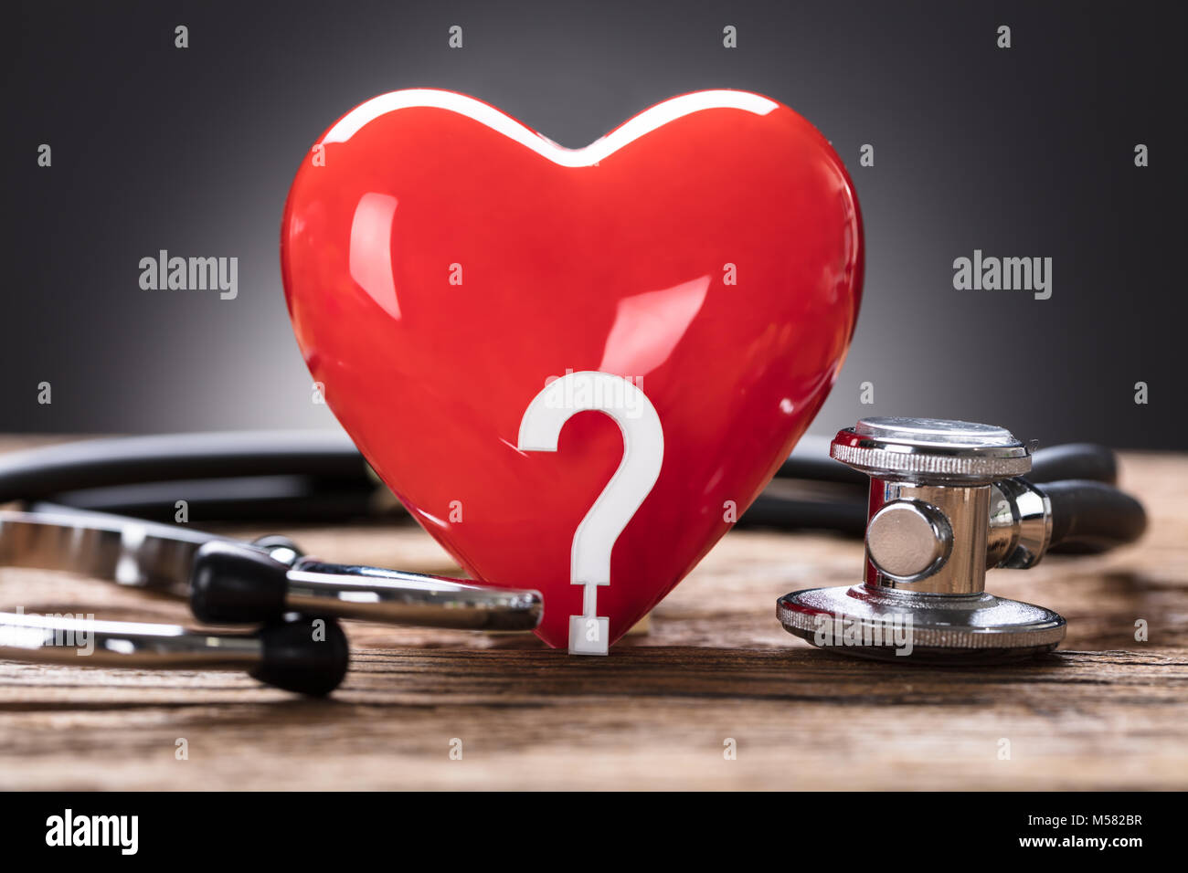 Vista dettagliata del cuore rosso e il punto interrogativo con uno stetoscopio sul tavolo di legno Foto Stock