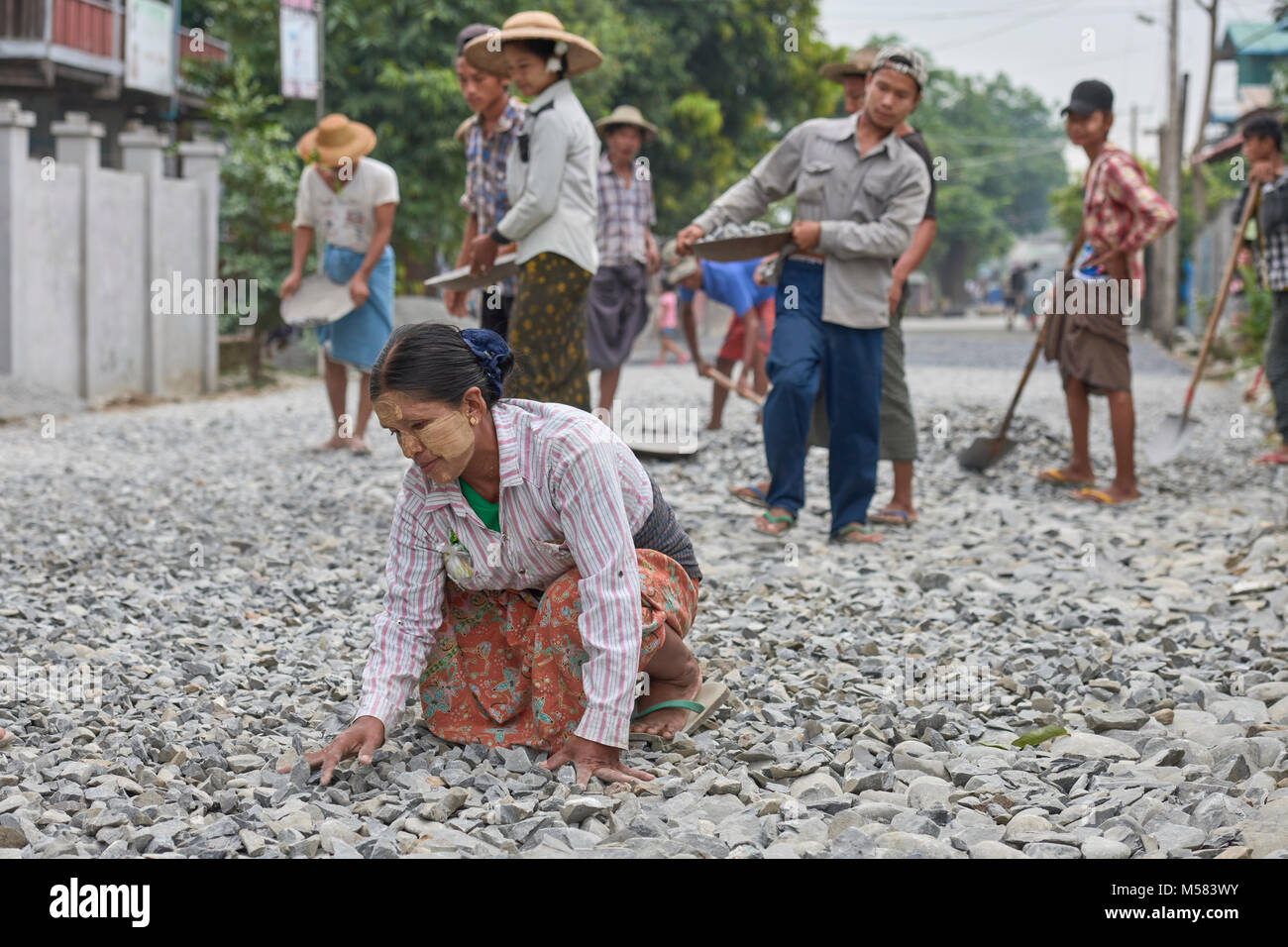 Una donna livelli rocce a mano come lavoratori a spianare la strada a Kalay, una città in Myanmar. La donna indossa thanaka, una pasta di cosmetici, sul suo viso. Foto Stock