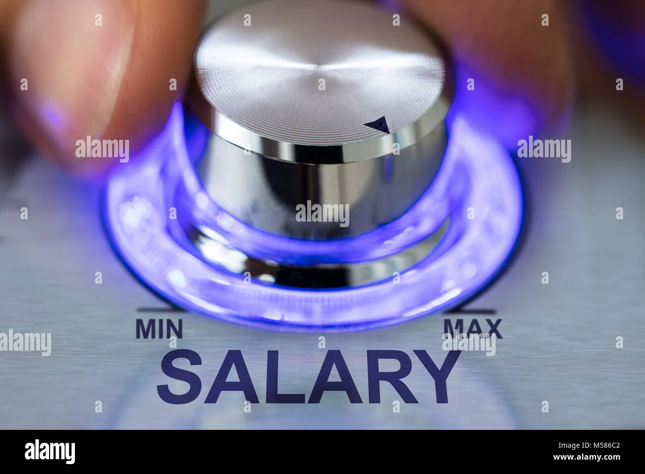 Immagine ritagliata della mano metallico ruotando la manopola illuminata dal testo di stipendio Foto Stock