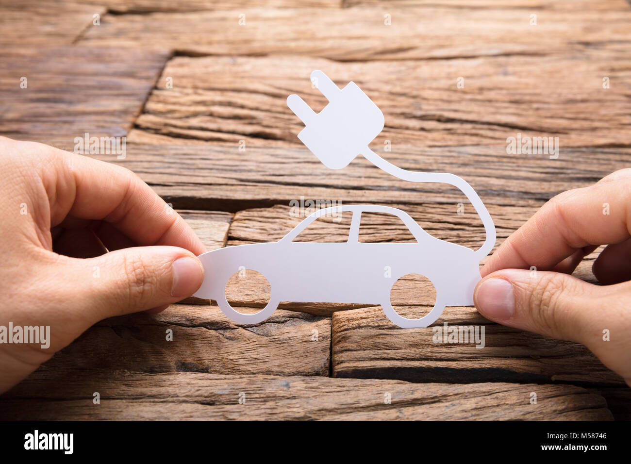 Immagine ritagliata di imprenditore il mano che tiene la carta auto elettriche al tavolo di legno Foto Stock