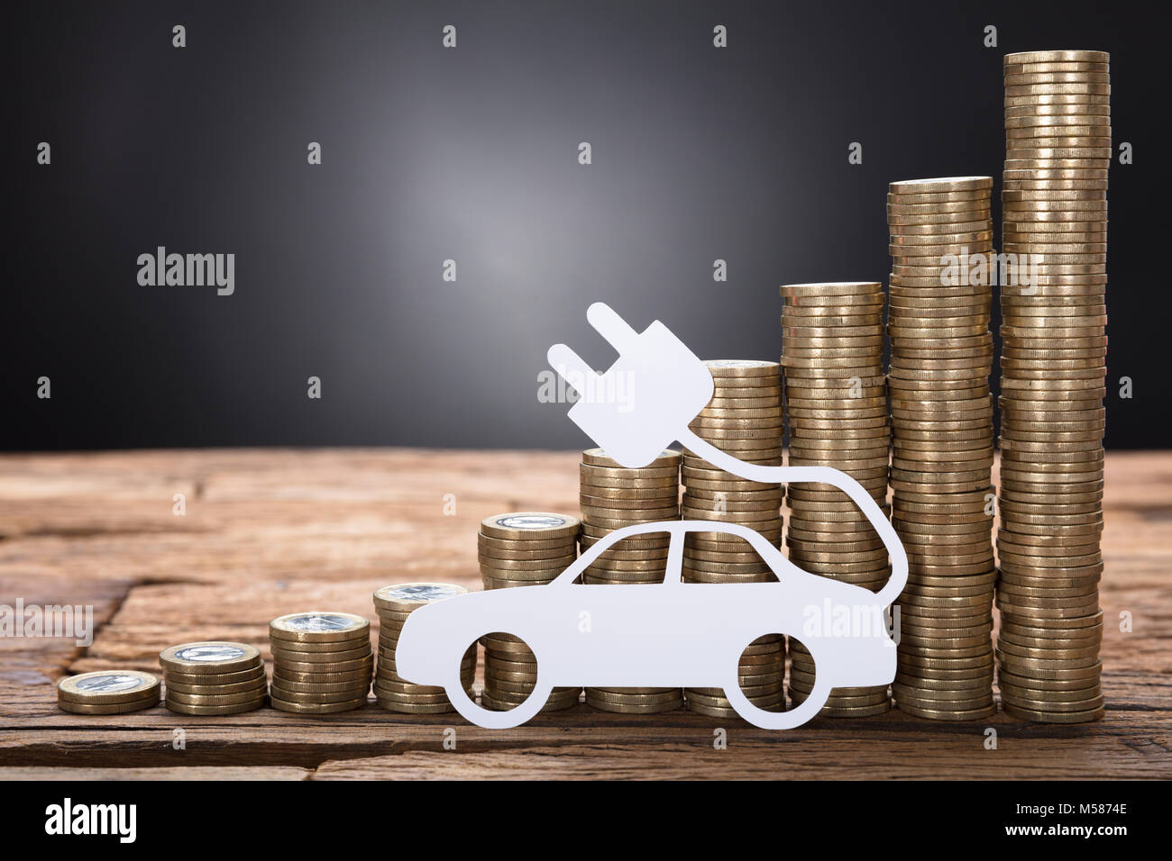 Primo piano della macchina elettrica contro le monete impilate su un tavolo di legno su sfondo nero Foto Stock