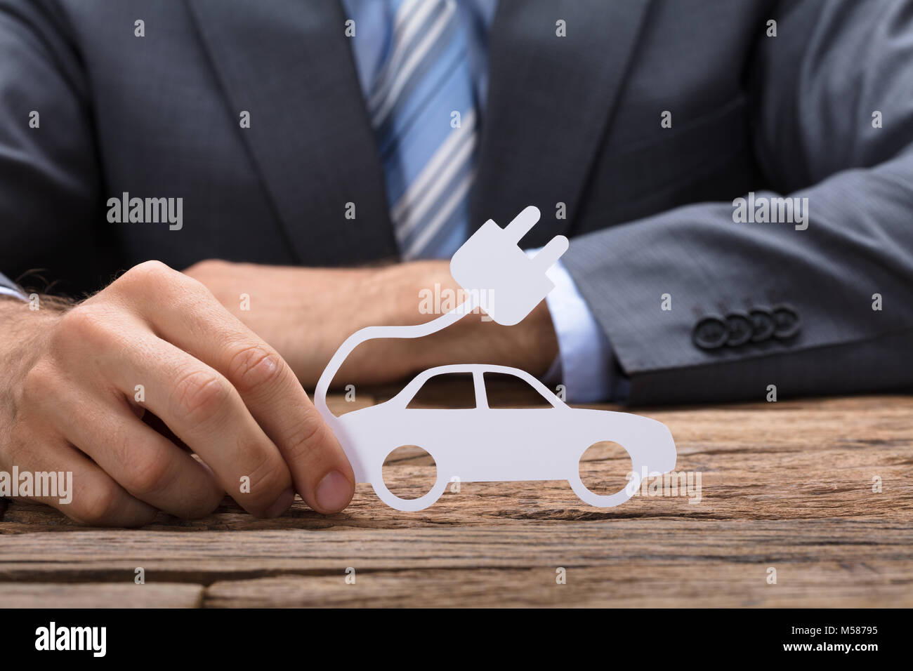 Sezione mediana di imprenditore tenendo la carta auto elettriche al tavolo di legno Foto Stock
