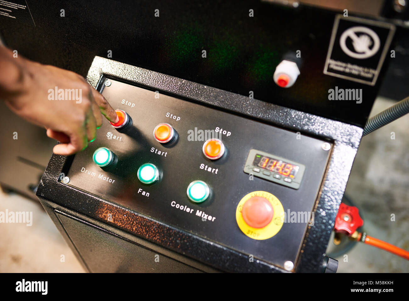 La Mano Nera occupato spingendo il pulsante rosso sul piano industriale in cerca del pannello dello switch per una tostatura del caffè macchina Foto Stock