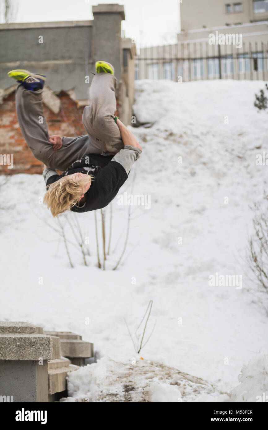 Adolescente capelli biondi guy formazione salto parkour flip nella coperta di neve park Foto Stock