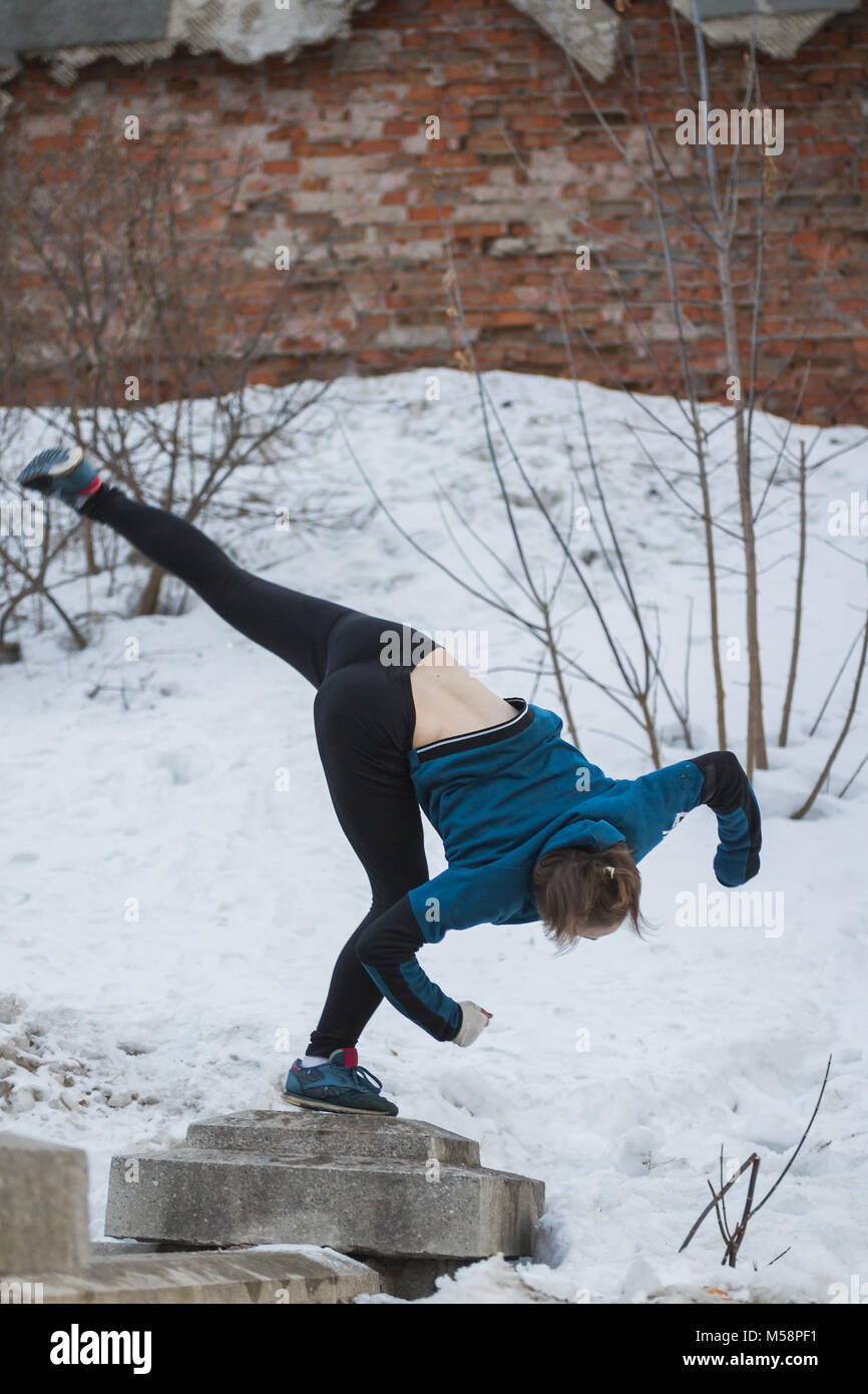 Teen girl jumping flip in snow winter park - free-run parkour concept Foto Stock