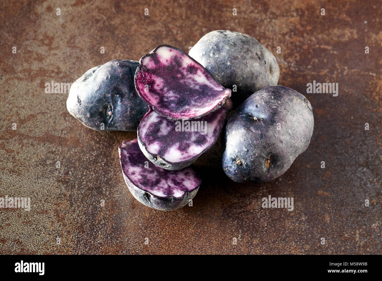 Fette di patate vitelotte, tre fette e tre patate intere su terreni accidentati sfondo scuro Foto Stock