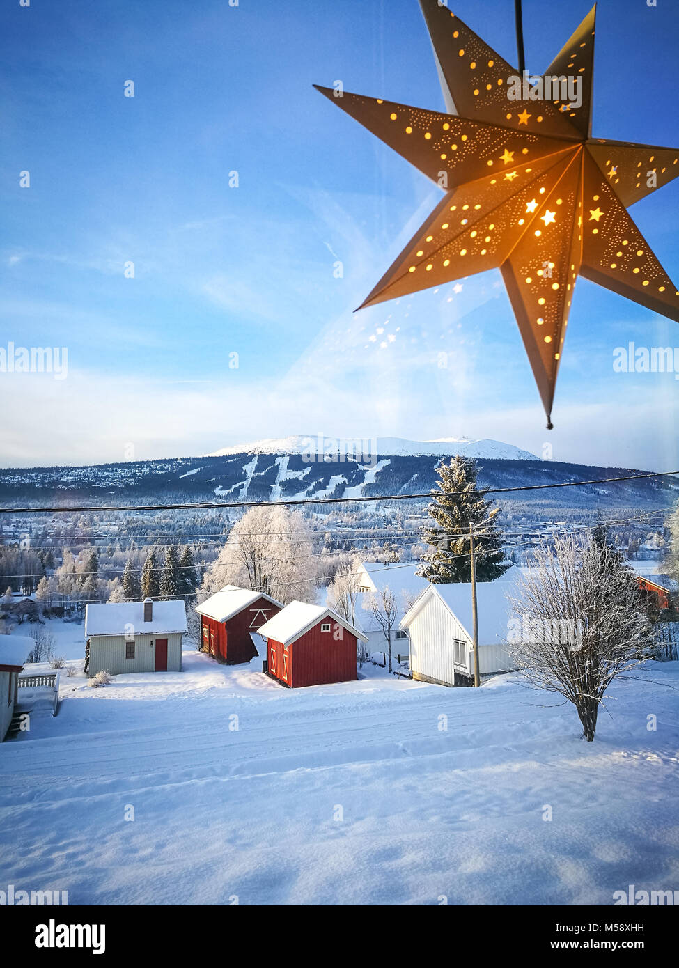 Grande avvento star ornamento colpo da dentro casa, una finestra che si affaccia sul Trysil e Trysilfjellet ski resort. Piccole case coloniche in primo piano. Foto Stock