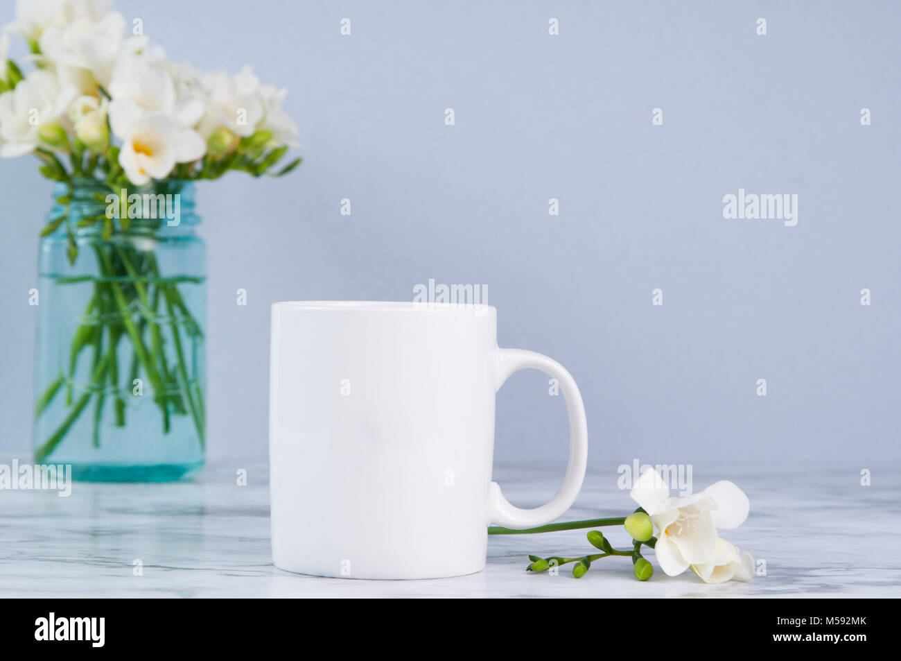 White 11oz mug mock up con fressia bianco fiori in blu di un vasetto di vetro Foto Stock