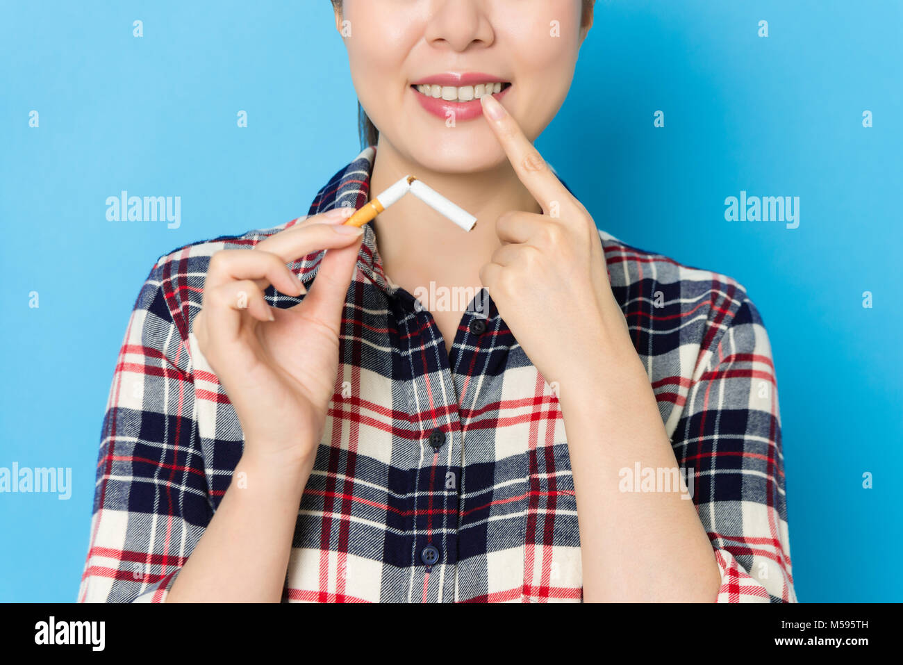 Sorridente donna elegante di puntamento dente Personale e azienda piegare sigaretta che mostra il cancro orale malati concetto quando ella in piedi di sfondo blu. Foto Stock