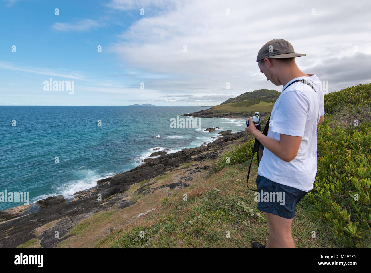 Un giovane uomo di scattare foto in prossimità dell'oceano con un analogo SLR Fotocamera Foto Stock