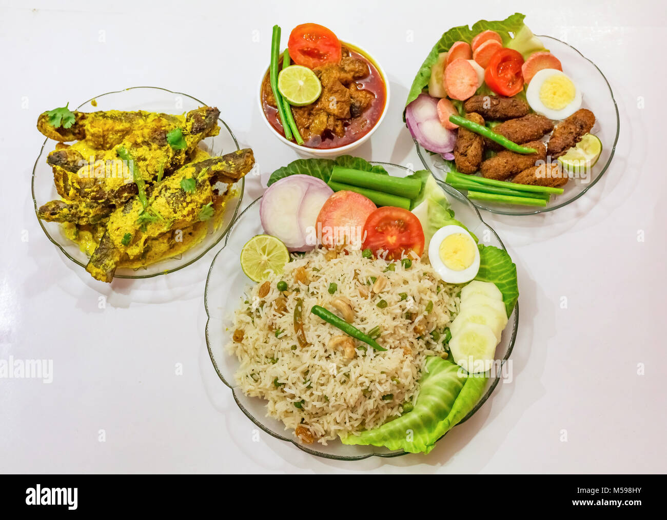 Popolare bengalese cibo indiano a piatti di riso fritto, bastoncini di pesce, carni di montone masala curry e tangra pesce al curry guarnita con insalata. Foto Stock