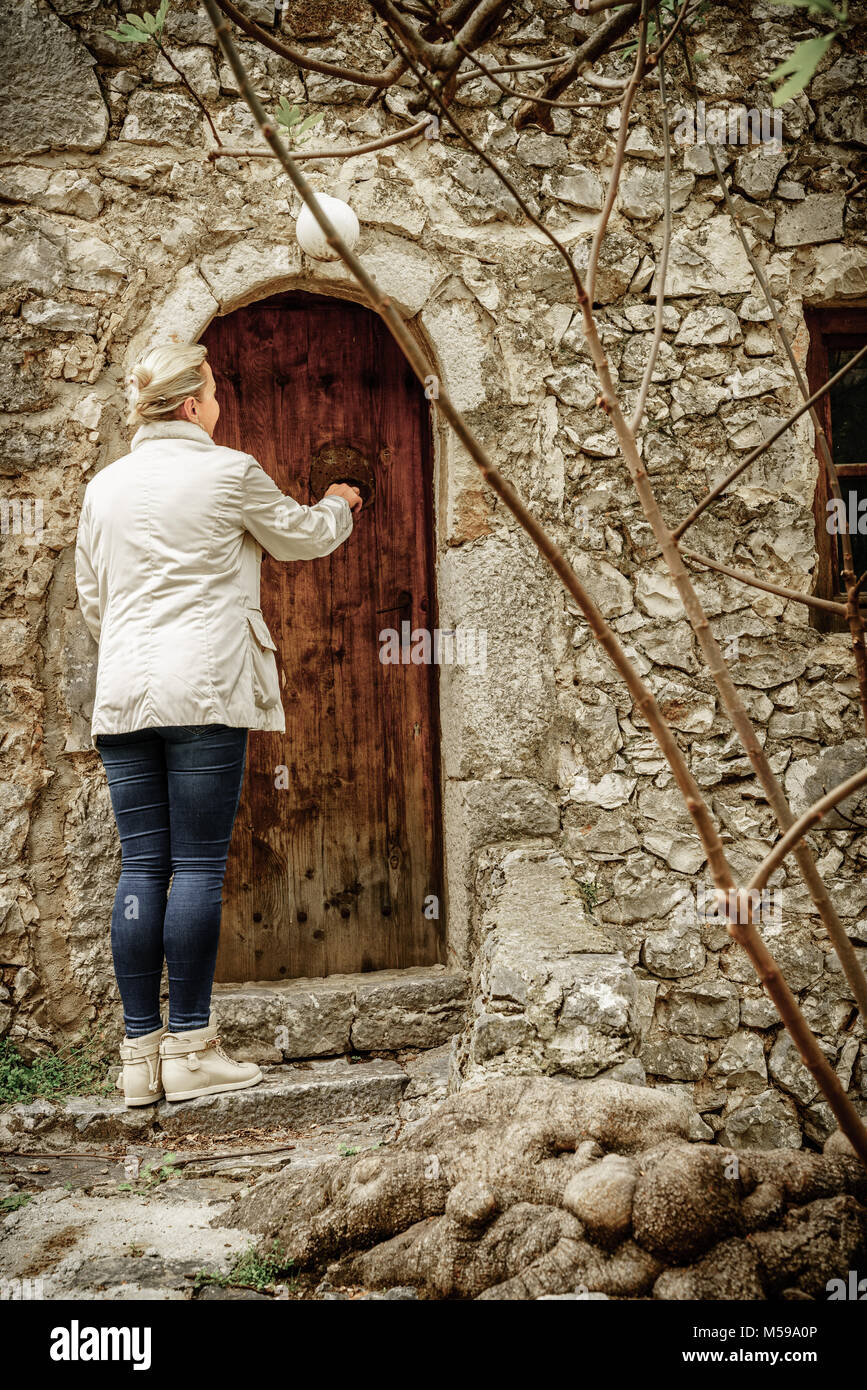 Una donna che bussa alla porta di una vecchia casa in un villaggio bosniaco Foto Stock
