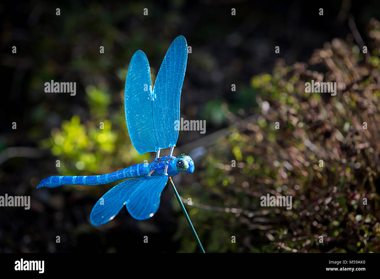 Modello ornamentale di una libellula blu su un filo con sbattimenti si avvolge in un giardino interno Foto Stock