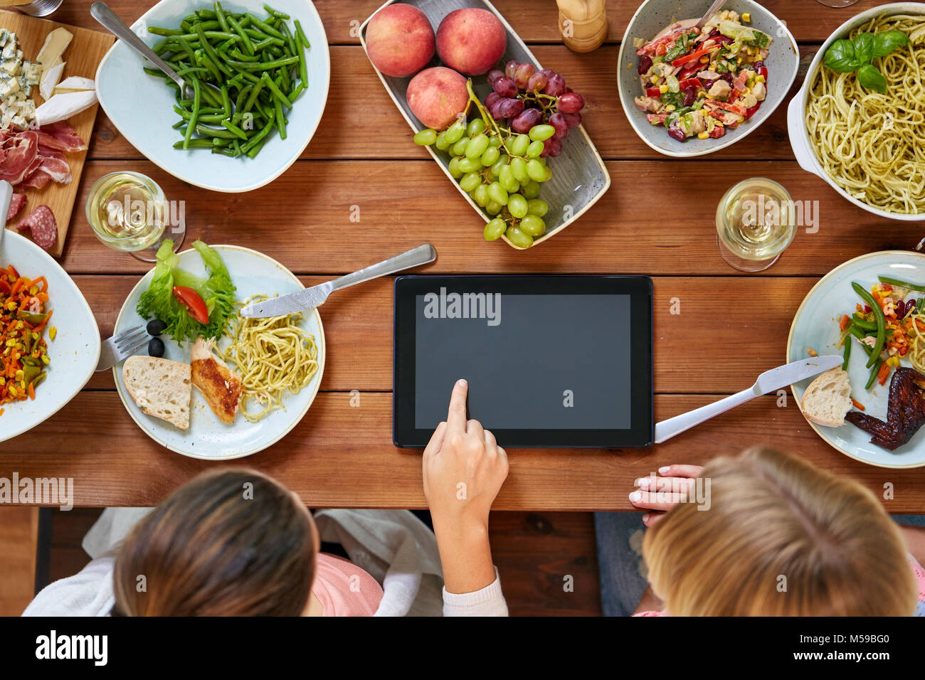 Le donne con tablet pc al tavolo pieno di cibo Foto Stock