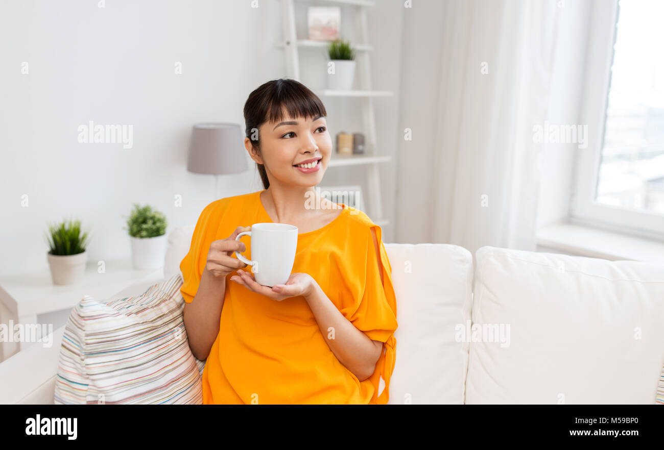 Felice donna asiatica bere il tè o il caffè a casa Foto Stock