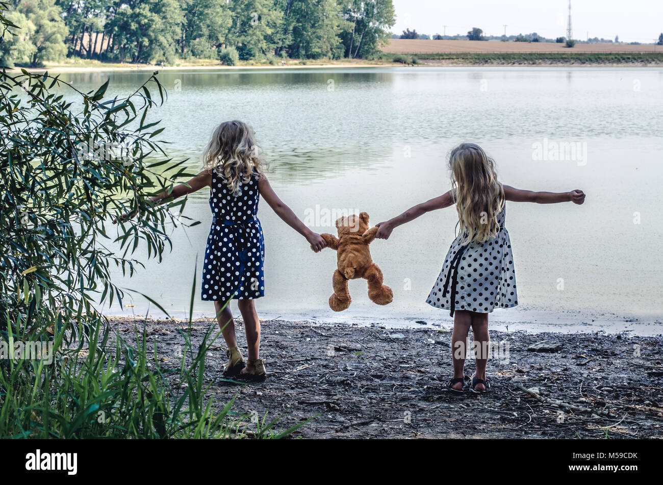 Due bambine con lunghi capelli biondi tenendo un orsacchiotto di peluche e giocattoli dancing Foto Stock