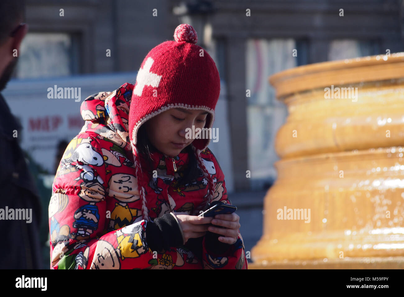 Una giovane donna orientale con il suo smartphone in strada in un freddo luminosa giornata invernale e caldo da indossare abbigliamento invernale, Trafalgar Square, Londra Foto Stock
