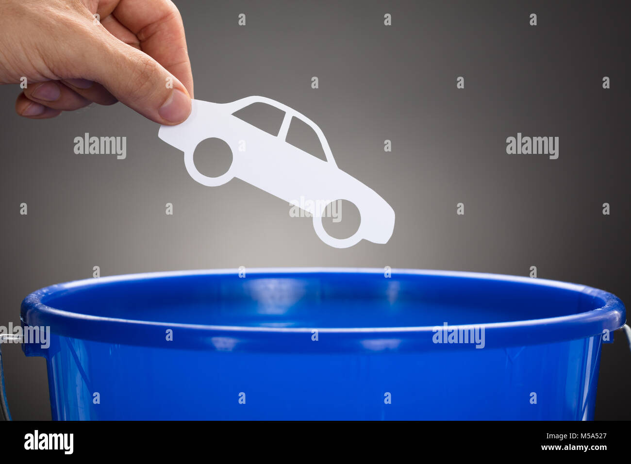 Ritagliate la mano di imprenditore di gettare la carta in auto blu benna contro uno sfondo grigio Foto Stock