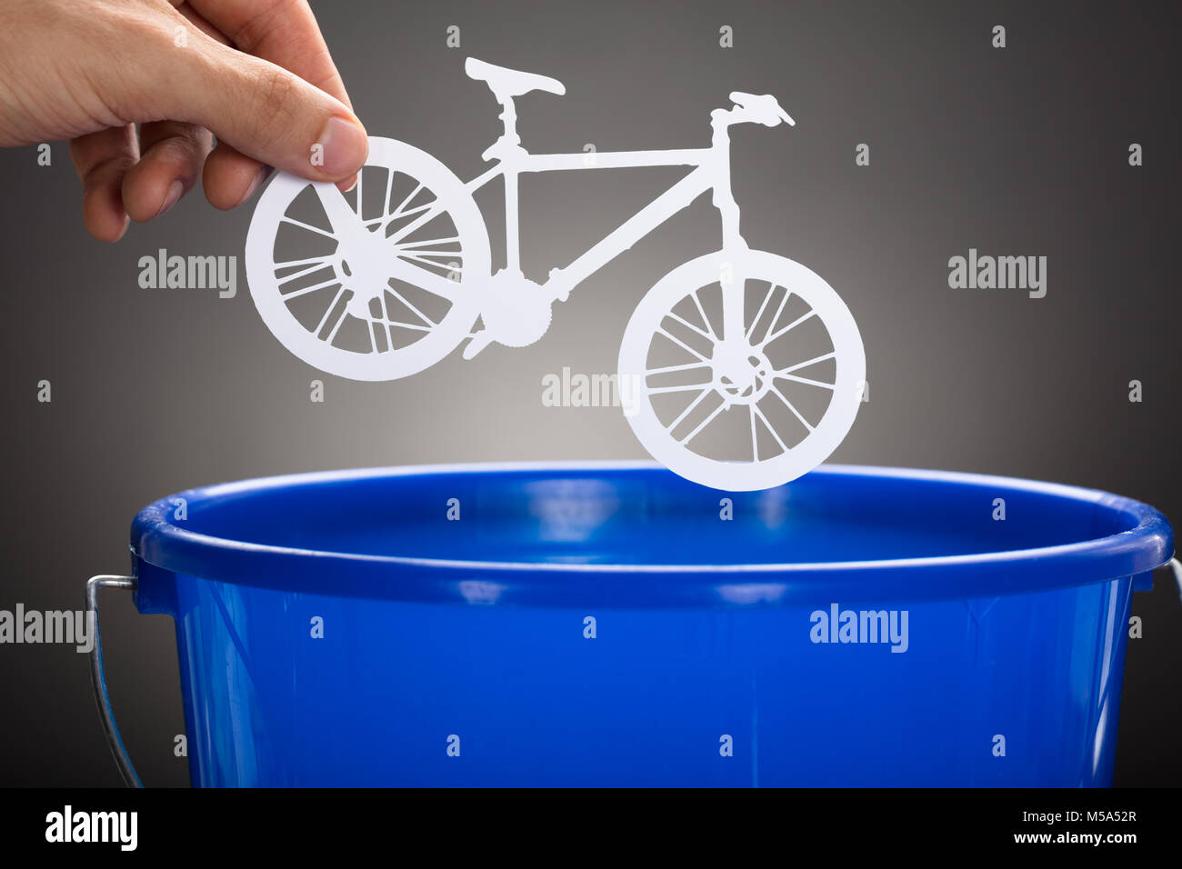 Ritagliate la mano di imprenditore di gettare la carta in bicicletta in blue benna contro uno sfondo grigio Foto Stock
