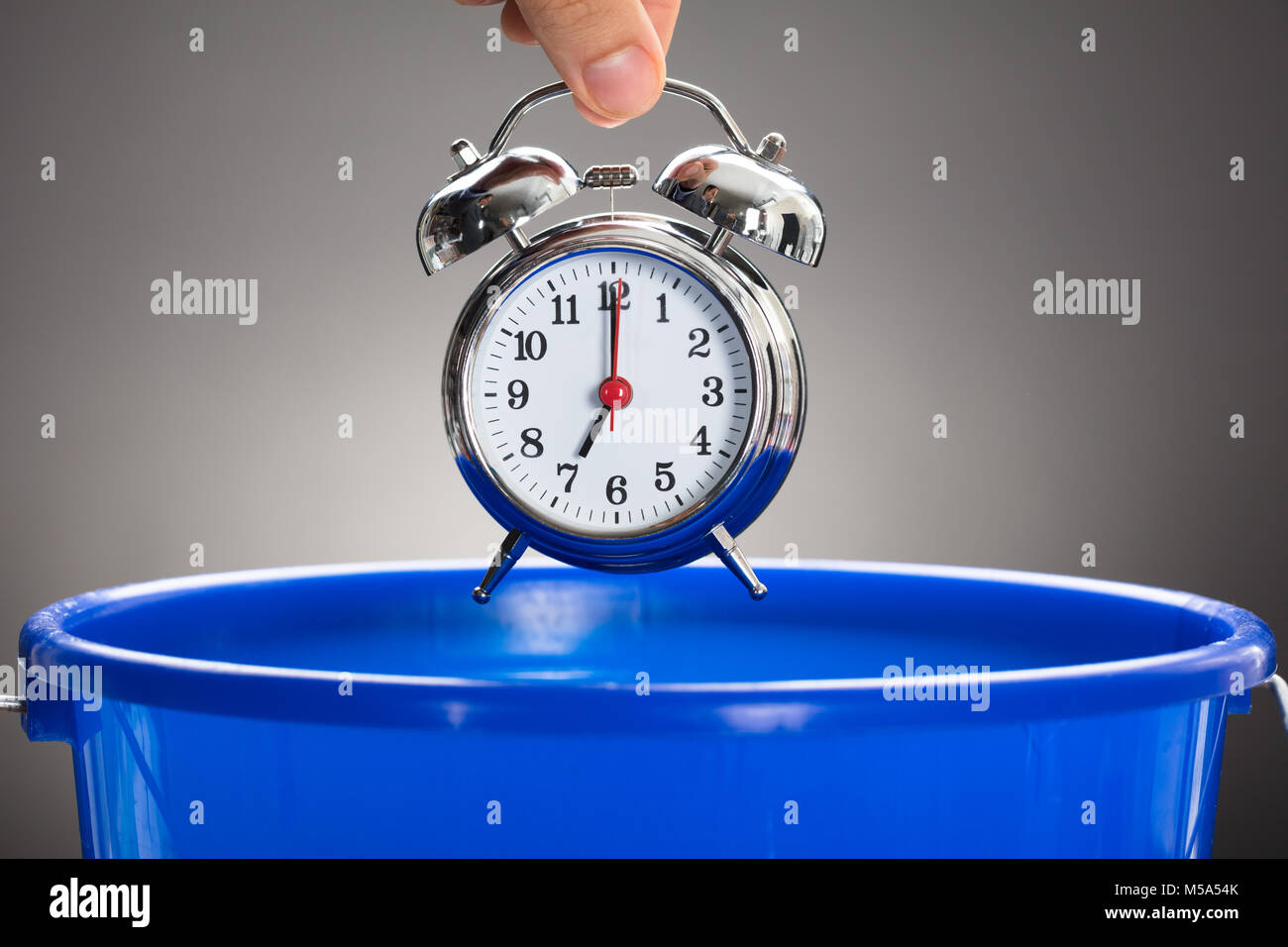 Ritagliate la mano dell'uomo d'affari gettando sveglia in blu la benna contro uno sfondo grigio Foto Stock