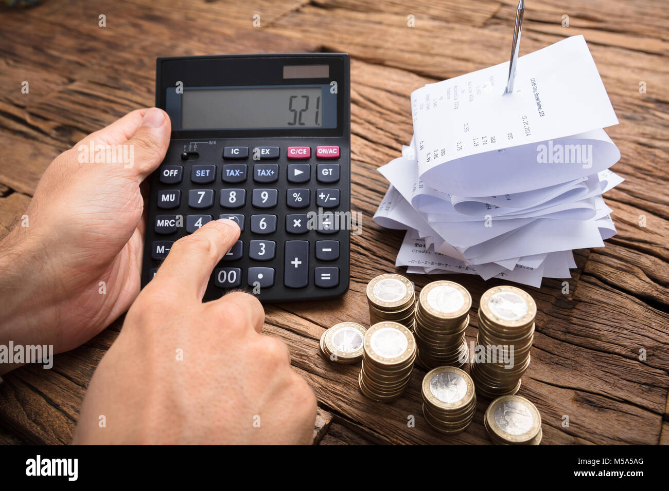 Immagine ritagliata di imprenditore utilizzando la calcolatrice con le monete e le fatture su un tavolo di legno Foto Stock