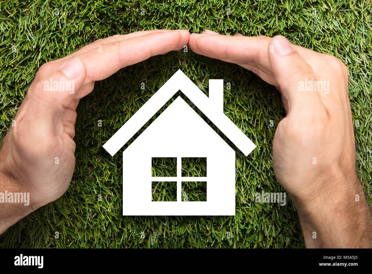 Direttamente sopra il colpo di imprenditore il mani di copertura casa carta sull'erba Foto Stock