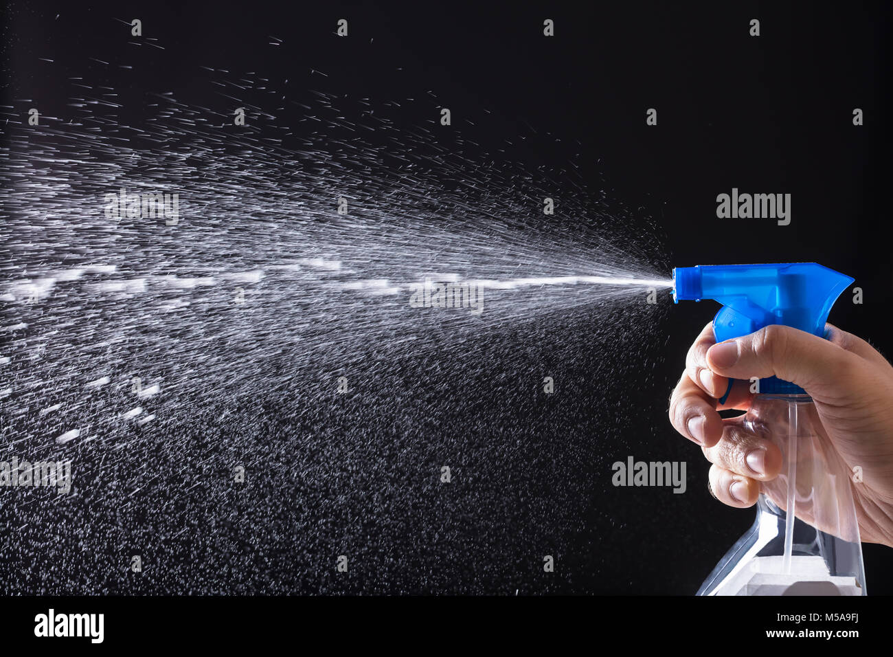 Mano umana la spruzzatura di acqua con la bottiglia spray su sfondo nero Foto Stock