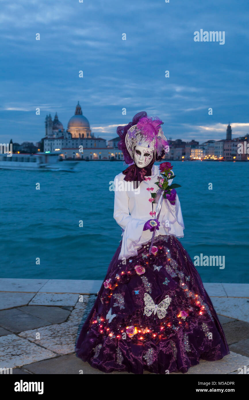 Il Carnevale di Venezia Costmes, Venezia, Veneto, Italia di notte con una donna in costume classico adornata con luci incandescenti di fronte al Canale della Giudecca a Foto Stock